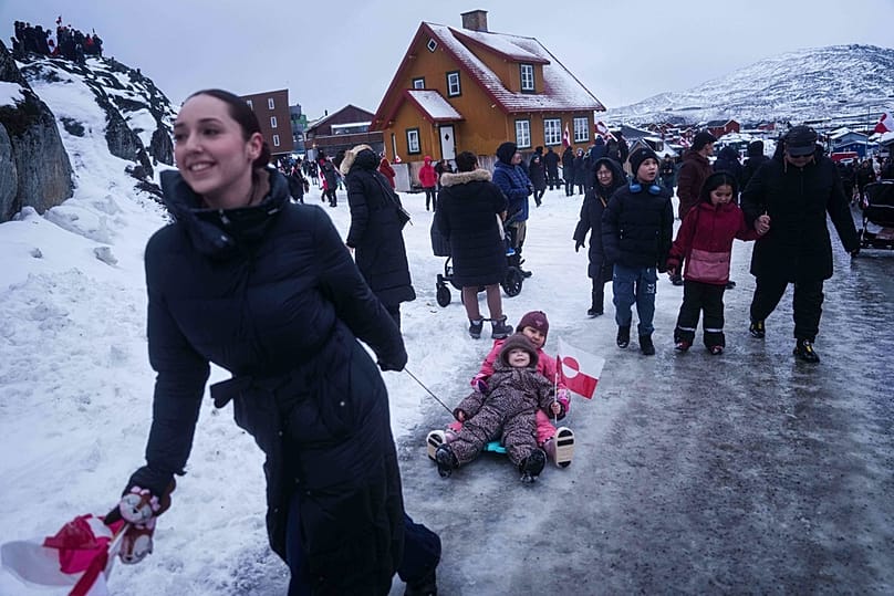 Grönland'ın Nuuk kentindeki ABD konsolosluğu önünde Trump'ın Grönland'a yönelik politikasını protesto eden bir kadın, çocuklarını kucakla çekiyor, 17 Ocak 2026.